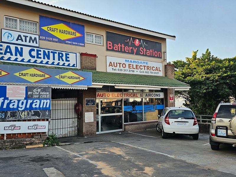 Front facade of a commercial retail center featuring multiple business signs, shopfront windows, and an attached parking area.