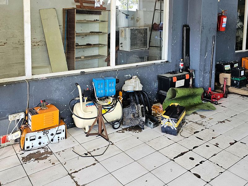 A utility or workshop space featuring tiled flooring, large glass windows, and wall-mounted fire safety equipment, currently used for storage and maintenance.