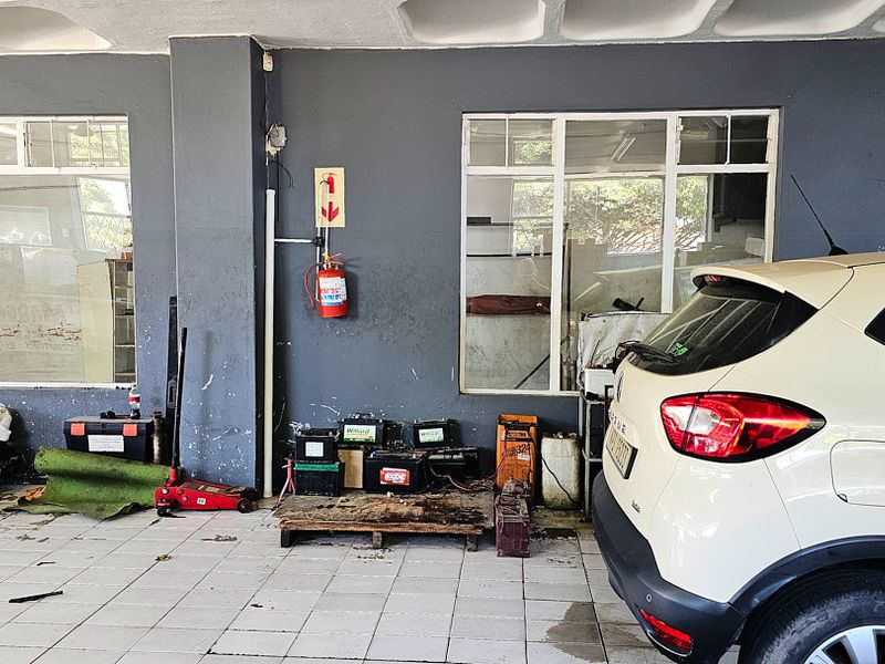 Commercial garage space featuring tiled flooring, large windows for natural light, and a wall-mounted fire extinguisher, suitable for workshop or storage use.