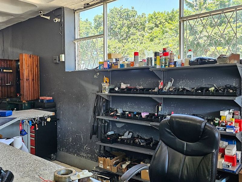 A functional commercial utility or workshop space featuring fixed metal shelving, a durable countertop, and security-fitted windows.