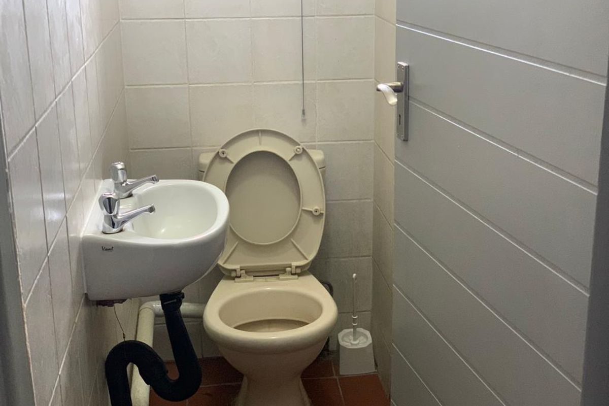 A compact guest bathroom featuring a wall-mounted basin and toilet with tiled finishes, requiring cosmetic updates to improve its overall condition.