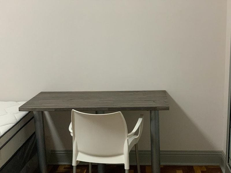 A bedroom space featuring parquet flooring and neutral wall finishes, currently set up with a desk and chair.