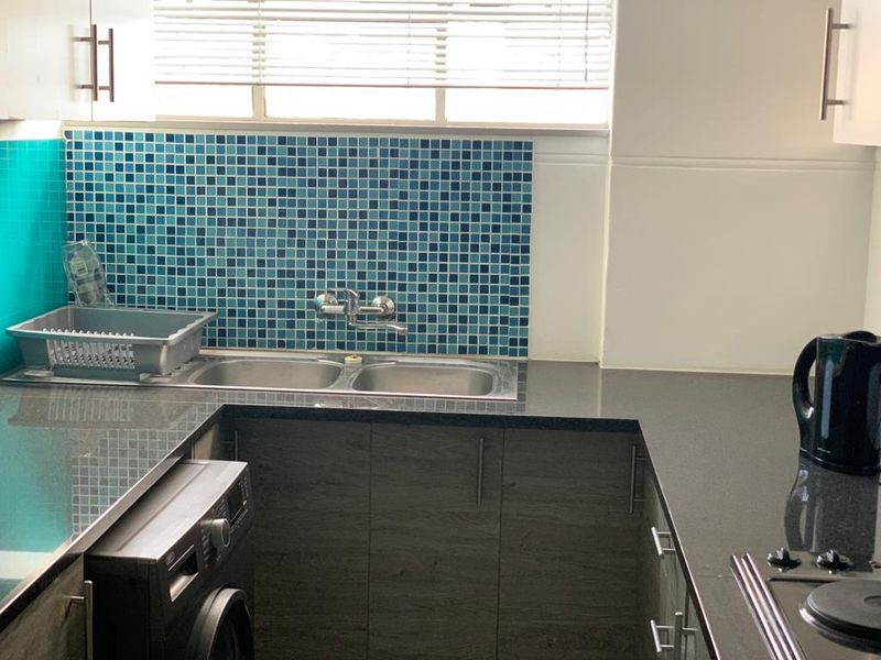 A functional kitchen featuring dark stone countertops, modern laminate cabinetry, a vibrant blue mosaic tile backsplash, and a double bowl stainless steel sink.