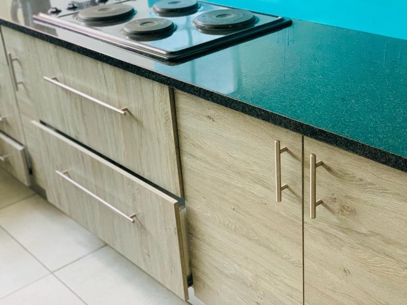 A kitchen area featuring wood-look laminate cabinetry, a dark stone countertop, and a built-in electric hob with ceramic floor tiling.