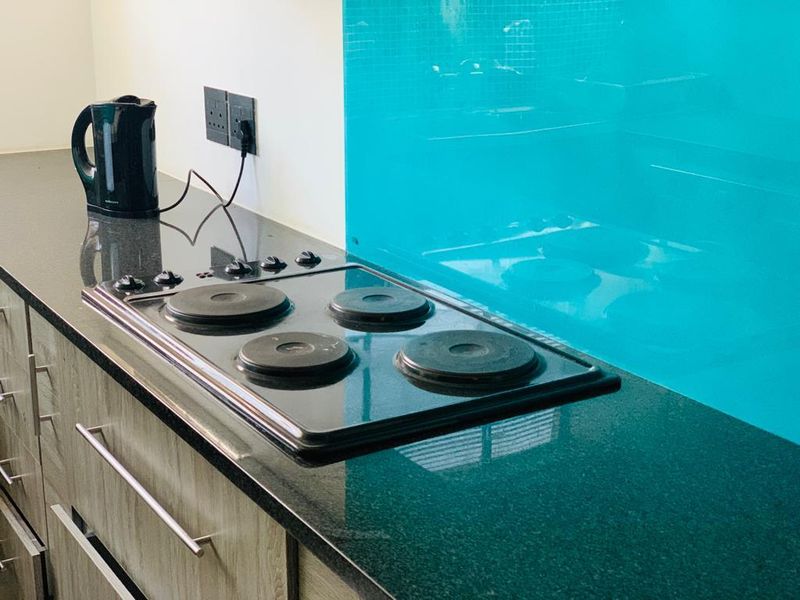 A kitchen workspace featuring a black electric hob, granite countertops, and a vibrant turquoise glass splashback with modern cabinetry.