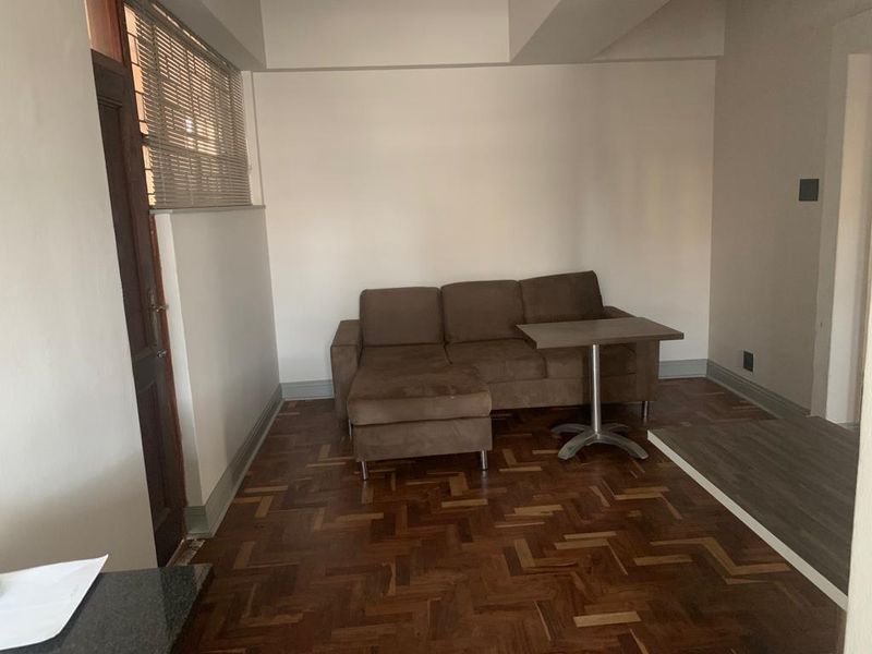 A living area featuring classic parquet flooring, a timber door, and venetian blinds, offering a neutral space ready for personalization.