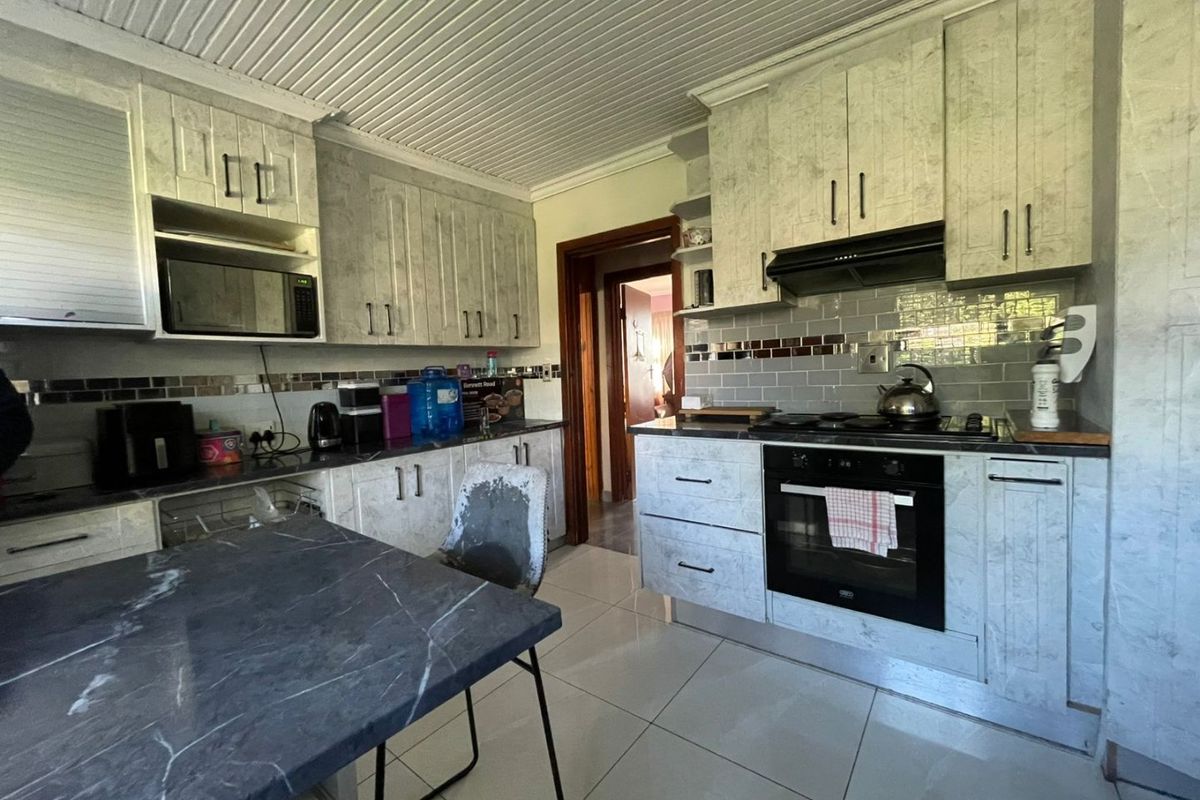 A functional kitchen featuring built-in cabinetry, a tiled backsplash, integrated oven, extractor fan, and durable floor tiles.