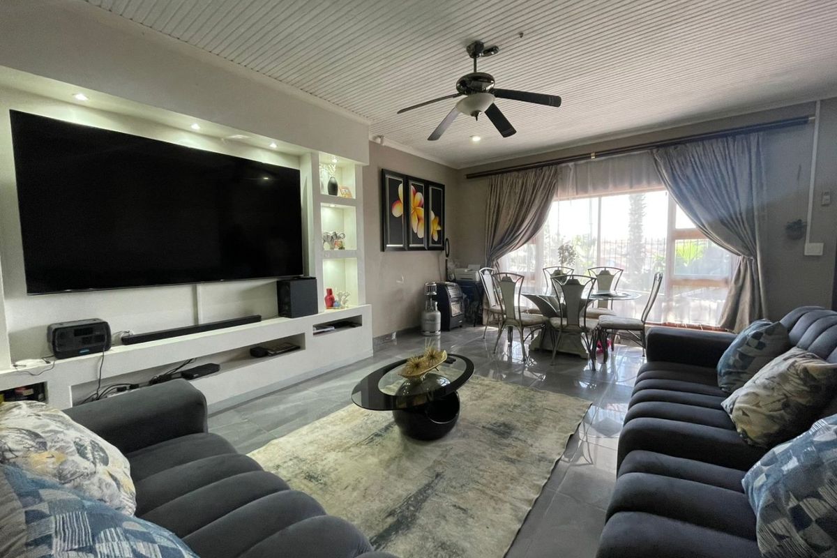 Open plan living and dining area featuring tiled floors, a built-in media wall with recessed shelving, and a ceiling fan.
