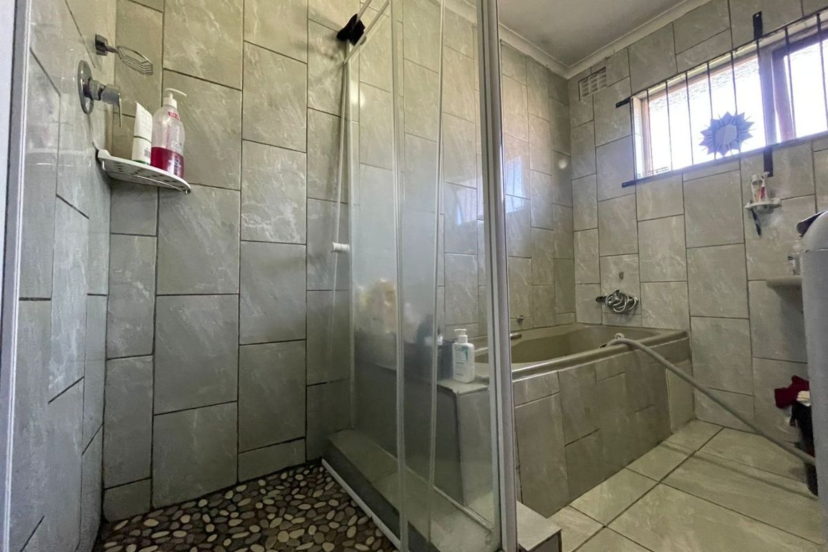 A functional bathroom featuring a combined shower and bathtub area with tiled finishes and a pebble-style shower floor.