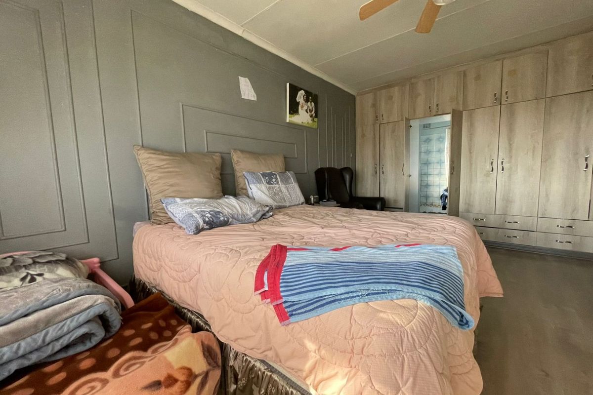 A bedroom featuring built-in wooden cupboards, a ceiling fan, and a grey panelled feature wall.