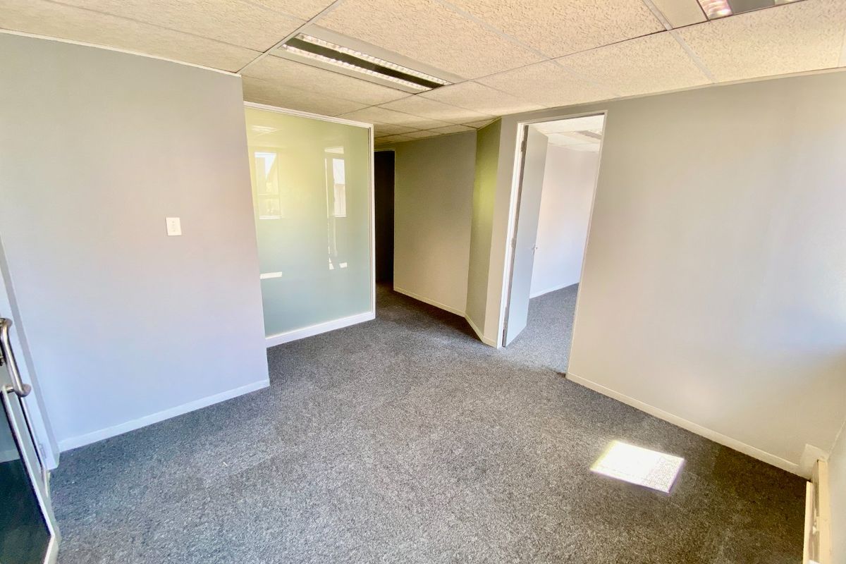 An empty commercial office space featuring grey carpeting, a suspended ceiling with recessed lighting, and a frosted glass partition wall.