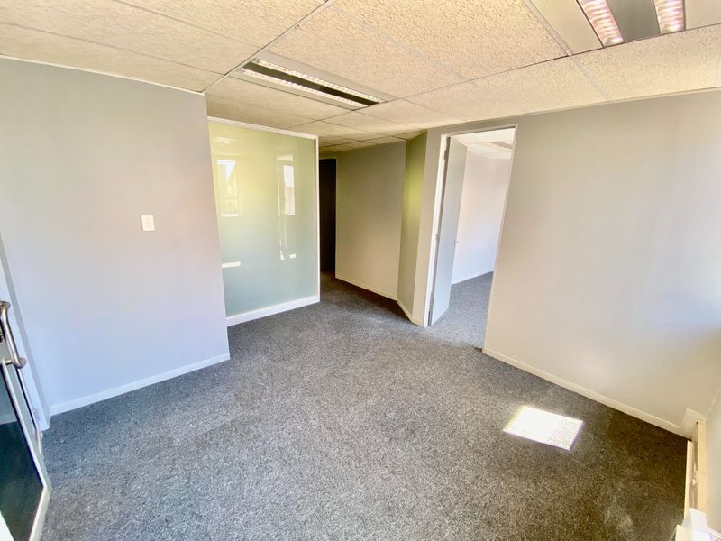 An empty commercial office space featuring grey carpeting, a suspended ceiling with recessed lighting, and a frosted glass partition wall.