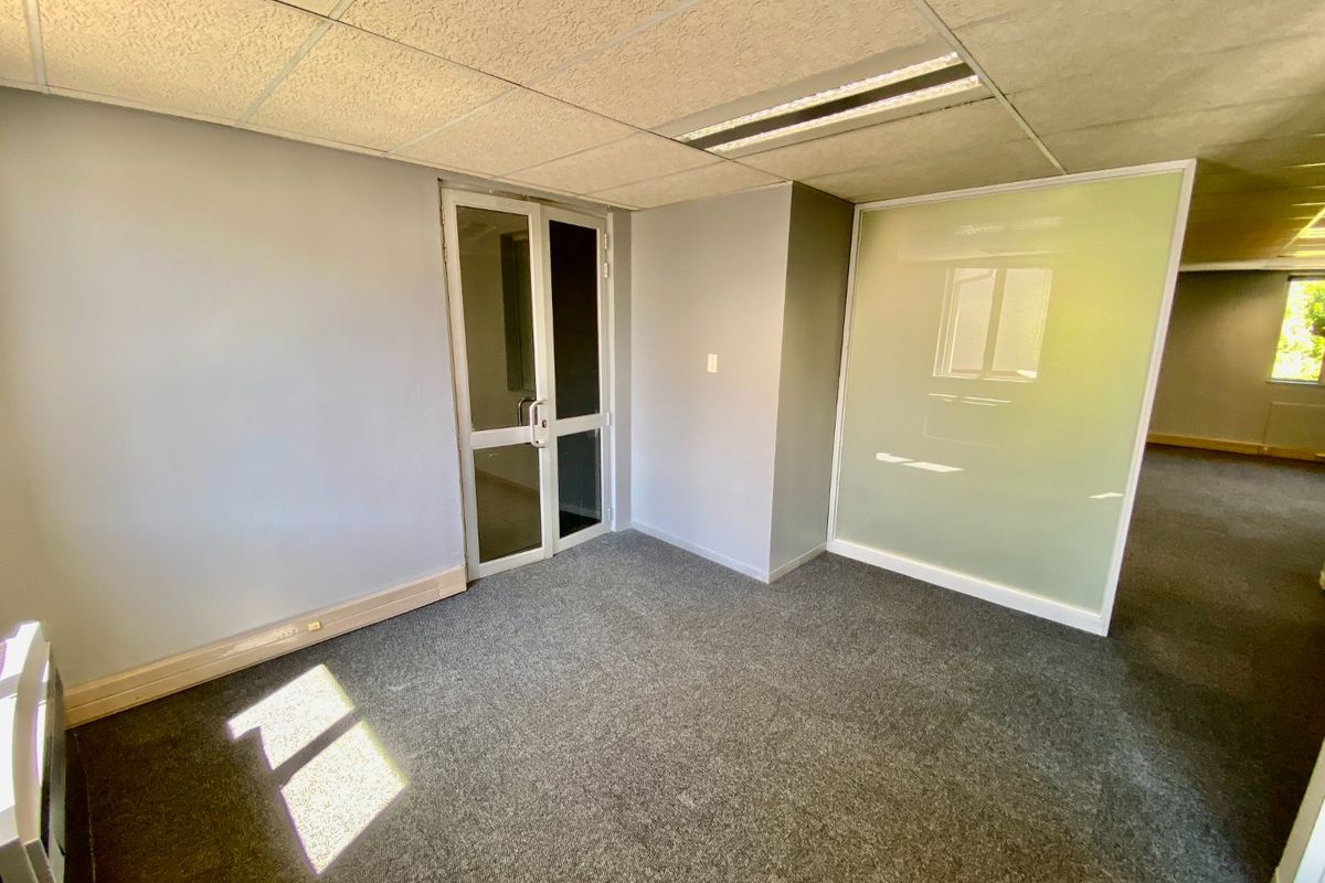 A vacant commercial office space featuring grey carpeting, a suspended ceiling with recessed lighting, and a modern frosted glass partition wall.
