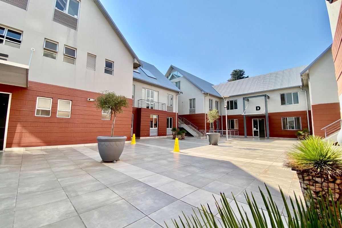 A well-maintained commercial courtyard featuring paved tiling, modern building facades with metal roofing, and access to multiple office units.