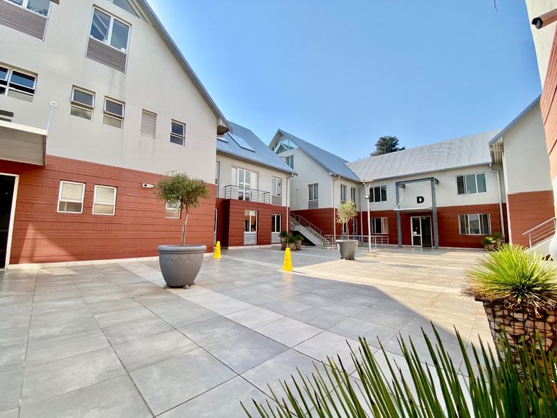 A well-maintained commercial courtyard featuring paved tiling, modern building facades with metal roofing, and access to multiple office units.