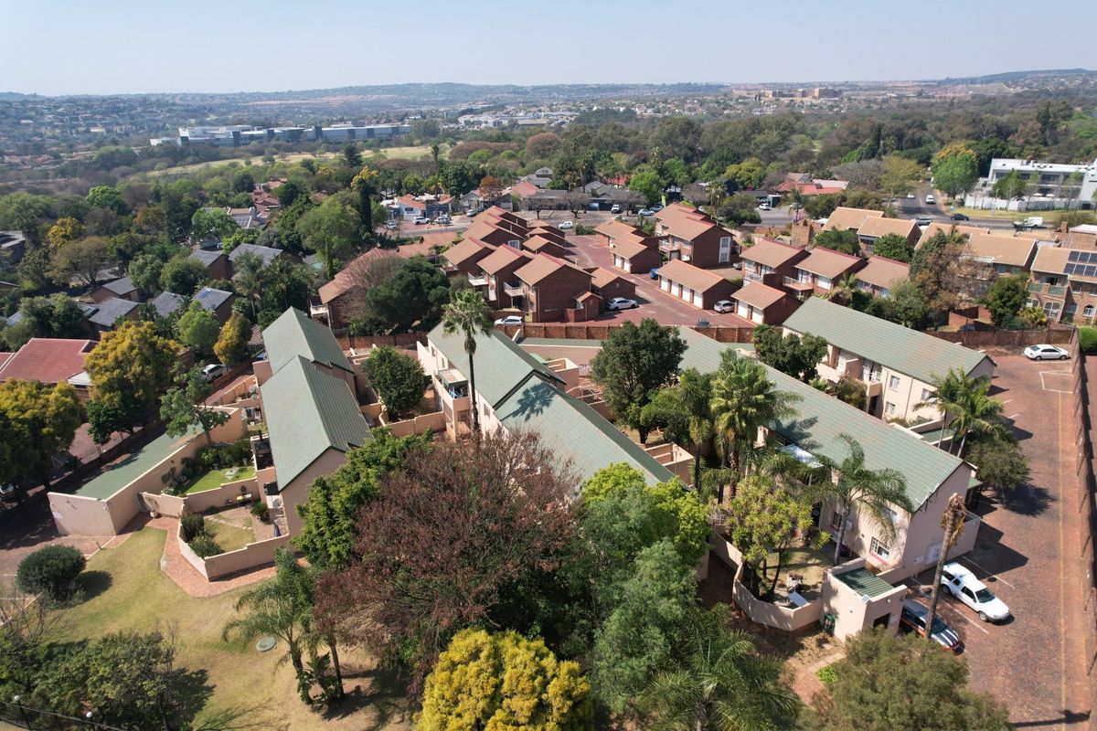 Aerial view of a residential apartment complex featuring multiple units with pitched roofs, paved driveways, and established garden areas.