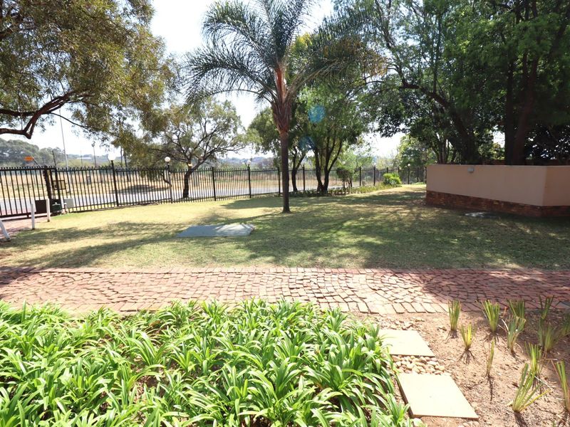 A spacious garden area featuring a brick paved pathway, established trees, and secure metal perimeter fencing.