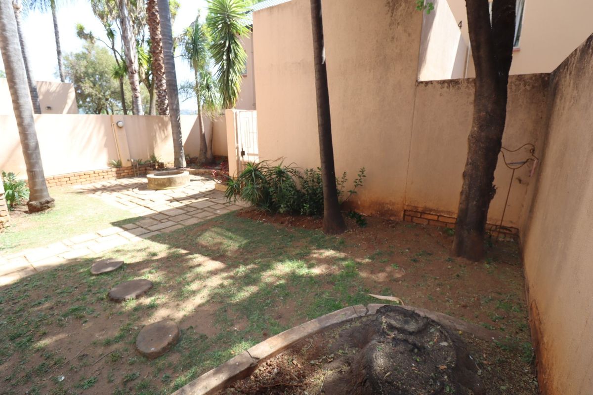 A private rear garden area featuring a paved patio, brick boundary walls, and established trees, offering potential for landscaping and outdoor improvement.