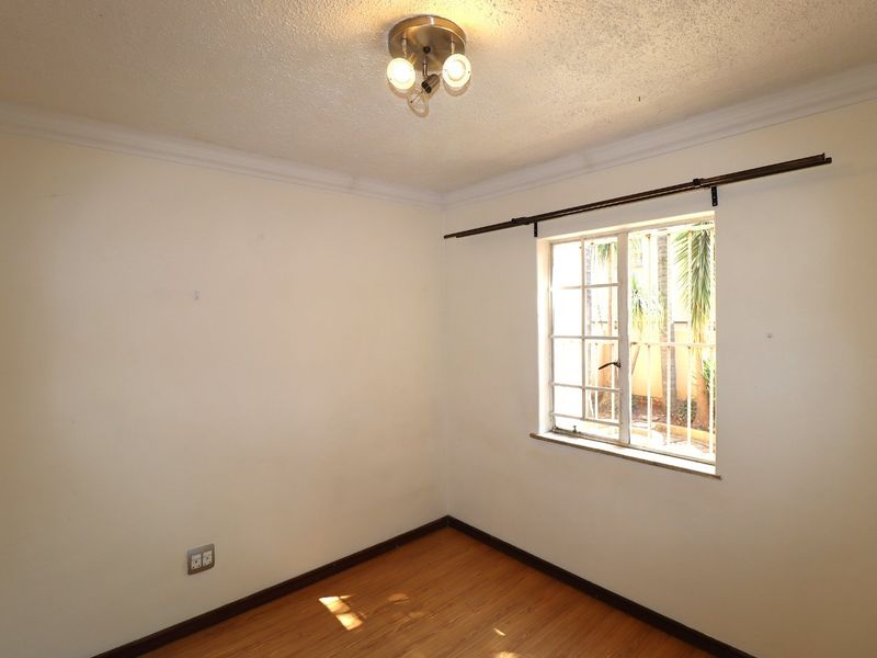 A bright, empty bedroom featuring laminate flooring, a window with security bars, and a central ceiling light fixture.