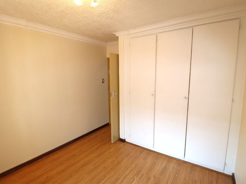 A vacant bedroom featuring laminate flooring, built-in cupboards, and classic cornice detailing, offering a clean canvas for personalization.