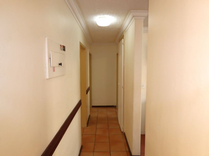 A clean, functional hallway featuring ceramic tile flooring, crown molding, and a dado rail, providing access to multiple rooms within the apartment.