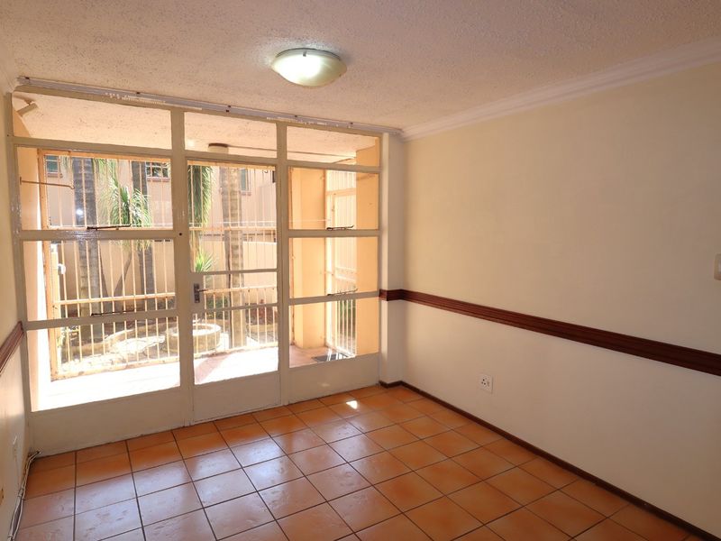An empty living area featuring ceramic tile flooring, chair rail molding, and large glass panels providing natural light and access to the outdoor space.