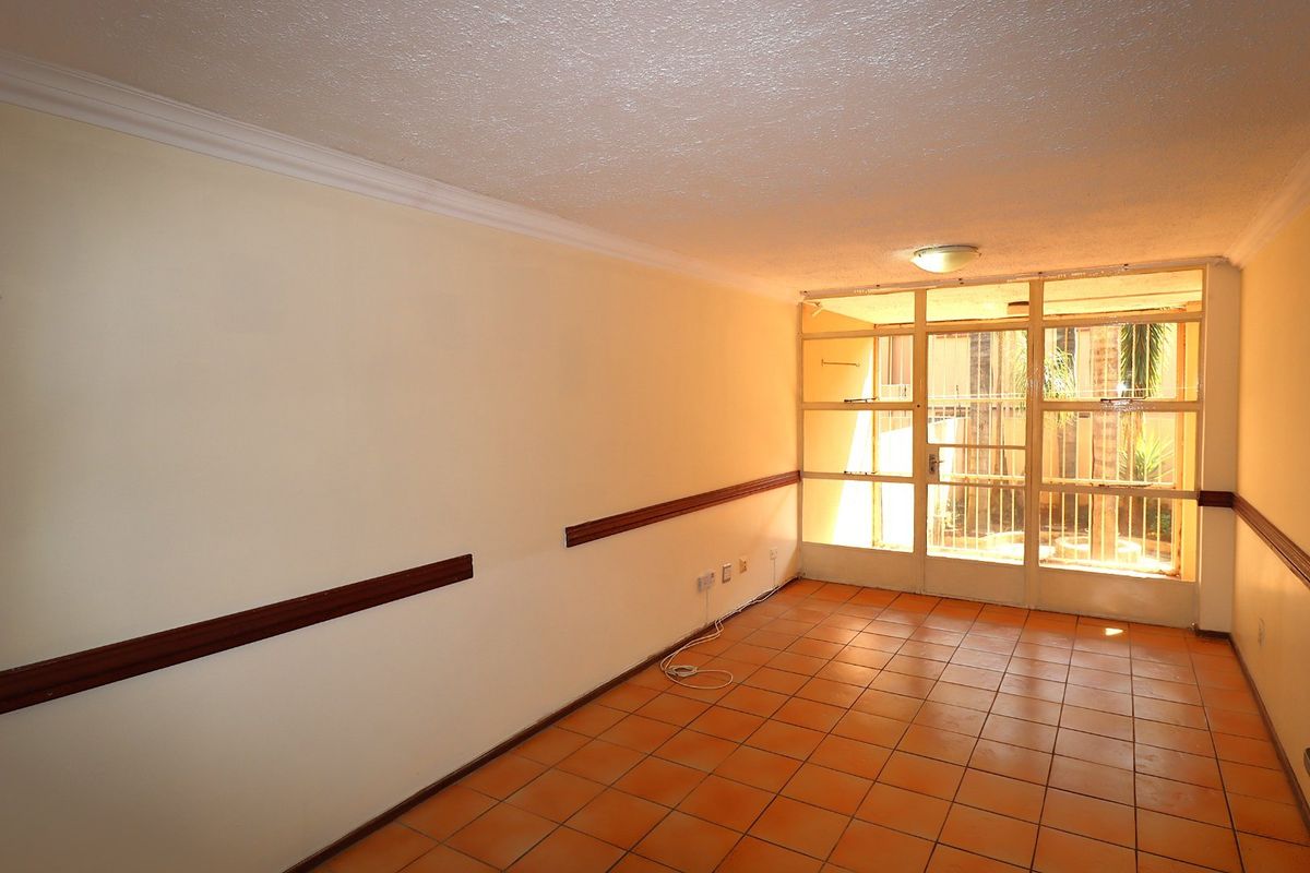 An empty living room featuring terracotta floor tiles, wooden dado rails, and a large glass panel window providing natural light.