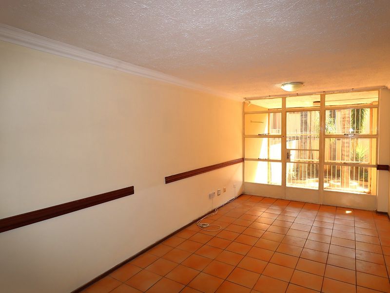 An empty living room featuring terracotta floor tiles, wooden dado rails, and a large glass panel window providing natural light.