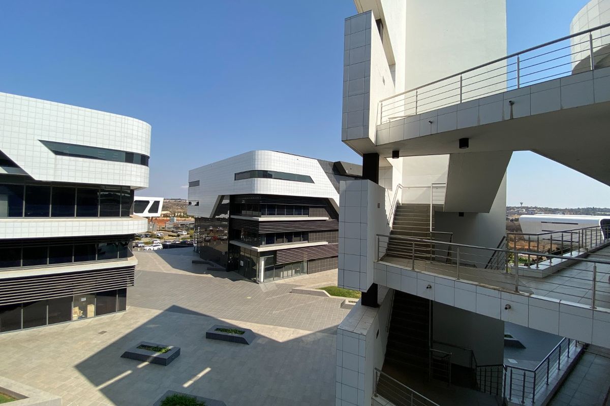 Modern commercial office complex featuring contemporary tiled facades, glass curtain walling, and an external staircase overlooking a paved courtyard area.