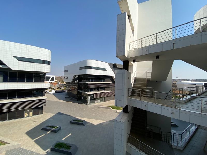 Modern commercial office complex featuring contemporary tiled facades, glass curtain walling, and an external staircase overlooking a paved courtyard area.