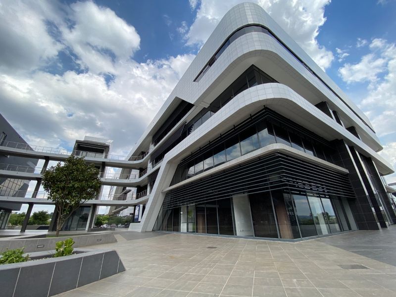 Modern commercial office building featuring a striking contemporary facade with extensive glass curtain walls, tiled exterior finishes, and elevated pedestrian walkways.