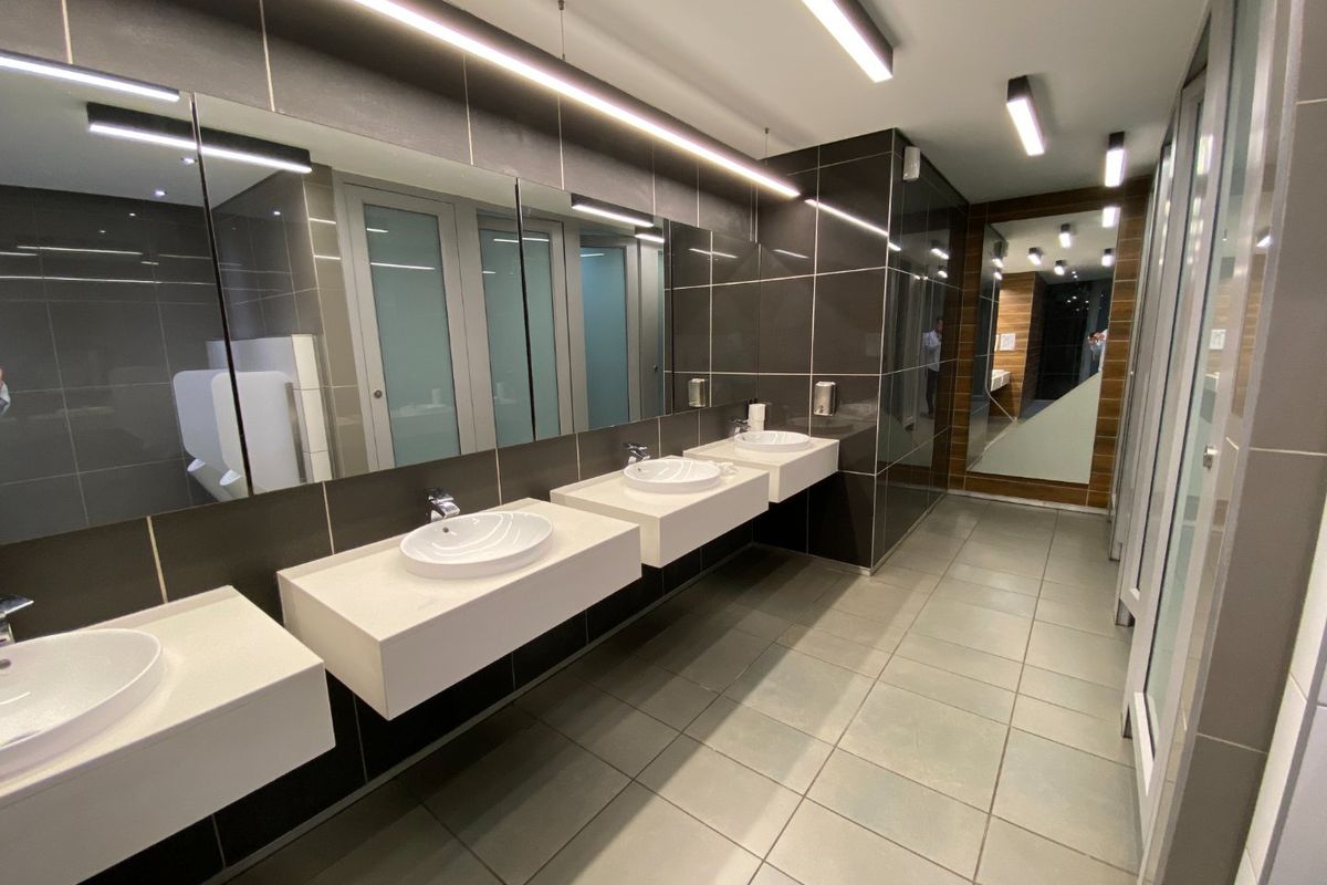 Modern commercial bathroom featuring multiple wall-mounted vanity basins, large mirrors, sleek linear lighting, and high-quality tiled finishes.