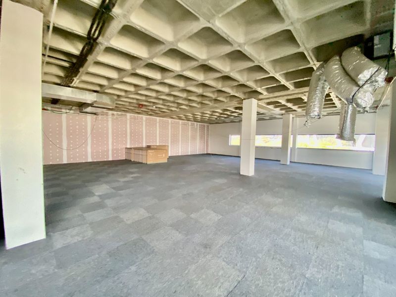An open-plan commercial office space featuring a waffle slab ceiling, exposed ductwork, and carpet tile flooring, currently in an unfinished shell condition.