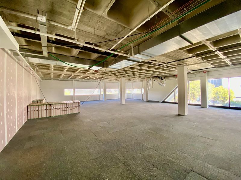 A large, open-plan commercial office space featuring an exposed waffle slab ceiling, structural columns, and expansive windows, currently in a shell condition.