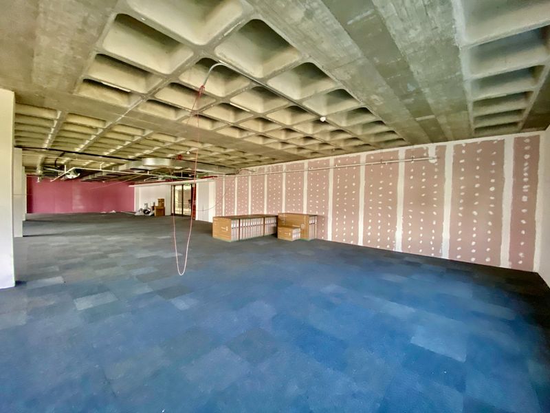 An open-plan commercial office space featuring a waffle slab ceiling, carpet tiles, and unfinished drywall partitions, currently in a shell condition.