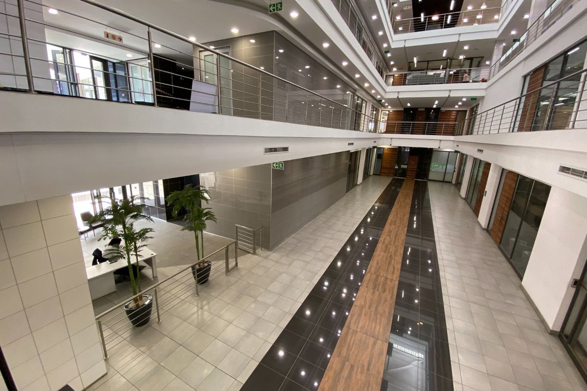 Spacious multi-level commercial atrium featuring modern tiled flooring, stainless steel balustrades, and glass-partitioned office suites with abundant natural light.