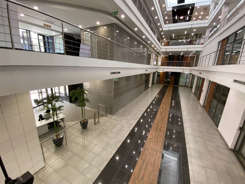 Spacious multi-level commercial atrium featuring modern tiled flooring, stainless steel balustrades, and glass-partitioned office suites with abundant natural light.