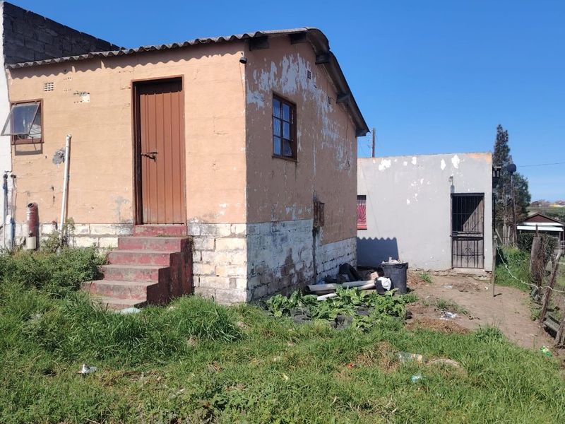 Rear view of a detached dwelling showing weathered exterior walls, concrete steps, and a secondary outbuilding structure on the property.