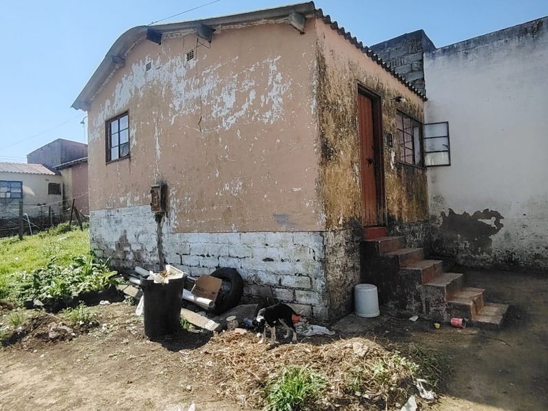 Rear view of a small detached dwelling showing significant exterior wear, peeling paint, and concrete steps requiring maintenance and restoration.