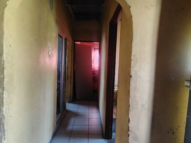 A narrow hallway featuring tiled flooring and an arched entryway, currently showing significant wear to the wall finishes.