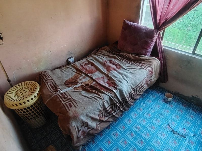 A small bedroom featuring tiled flooring and security bars on the window, currently showing significant wear to wall finishes and flooring.
