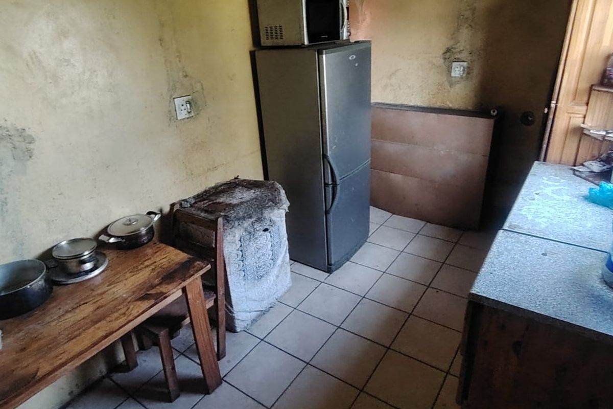 A small kitchen area featuring tiled flooring and significant wall surface deterioration, requiring renovation and cosmetic repairs to improve the space.