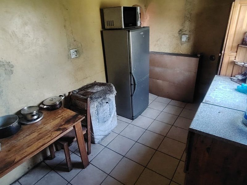 A small kitchen area featuring tiled flooring and significant wall surface deterioration, requiring renovation and cosmetic repairs to improve the space.