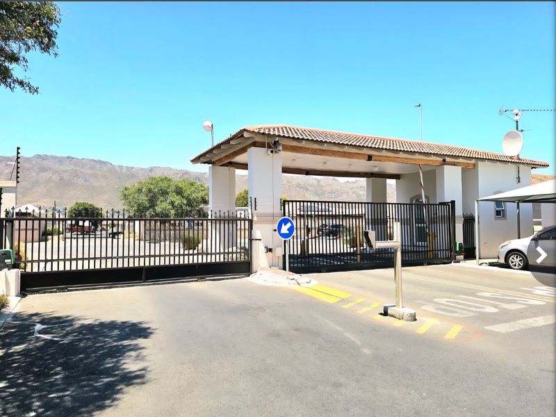 Secure gated entrance to the apartment complex featuring a guard house, automated security gate, and boom access control.