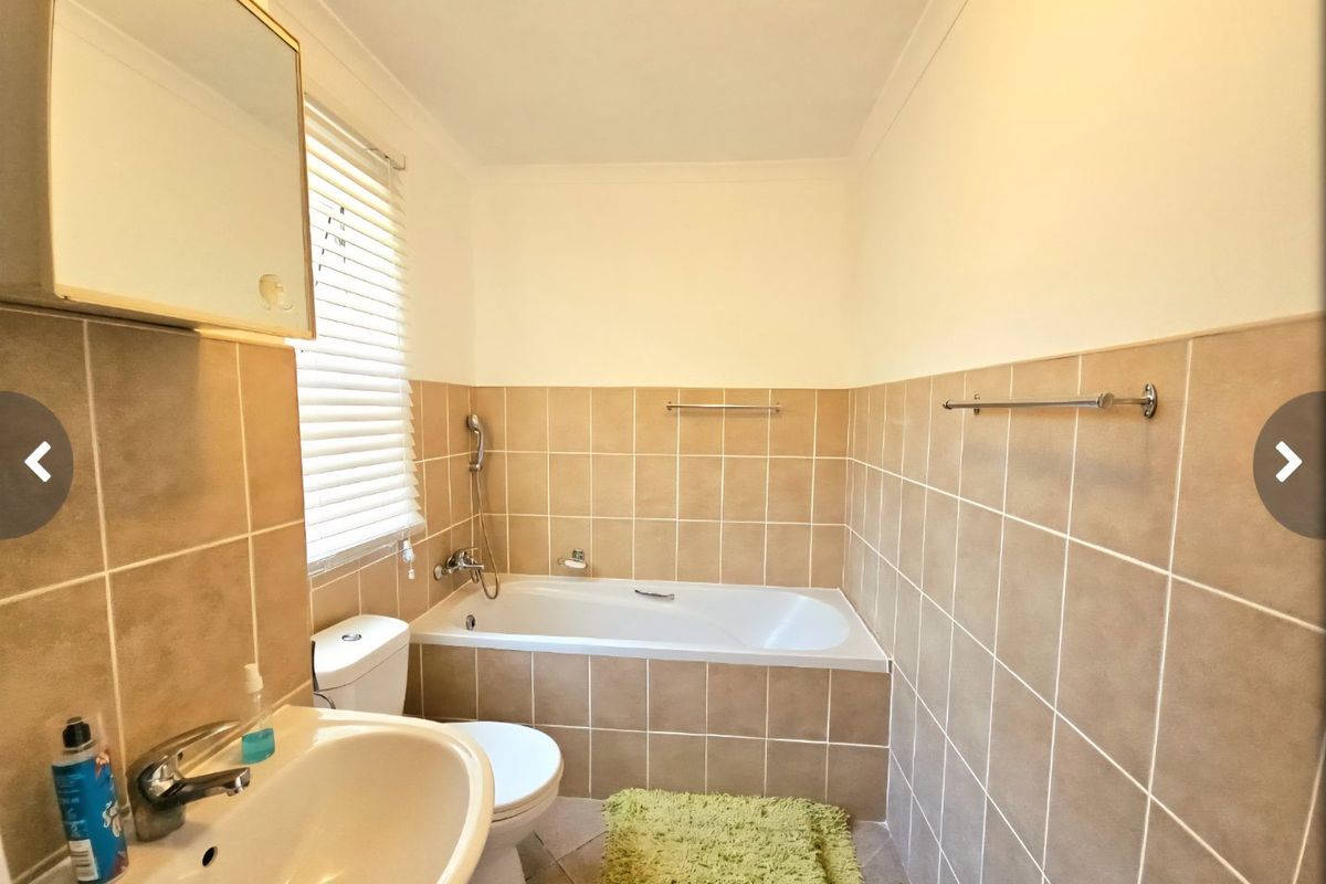 A functional bathroom featuring a built-in bathtub, pedestal washbasin, toilet, and neutral ceramic wall tiling with a medicine cabinet and towel rails.