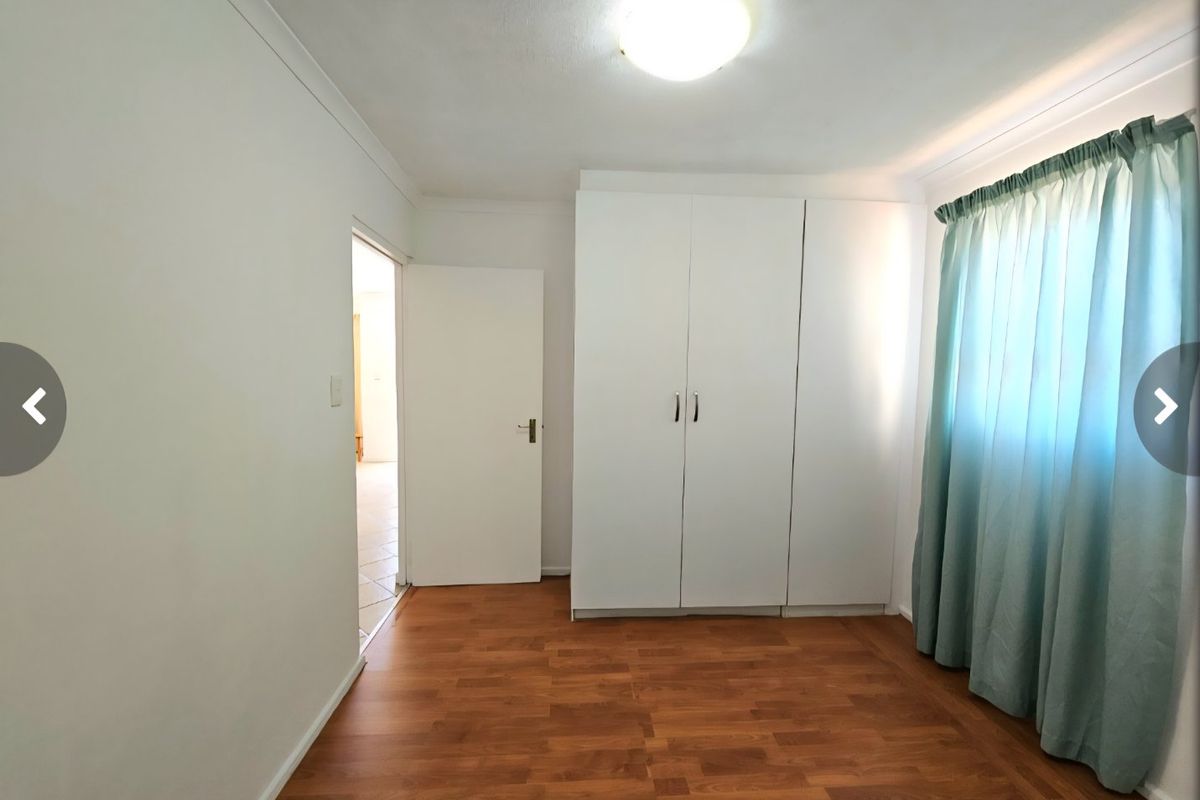 A bright, empty bedroom featuring laminate flooring, a built-in wardrobe, and a ceiling light fixture, offering a clean and neutral space.