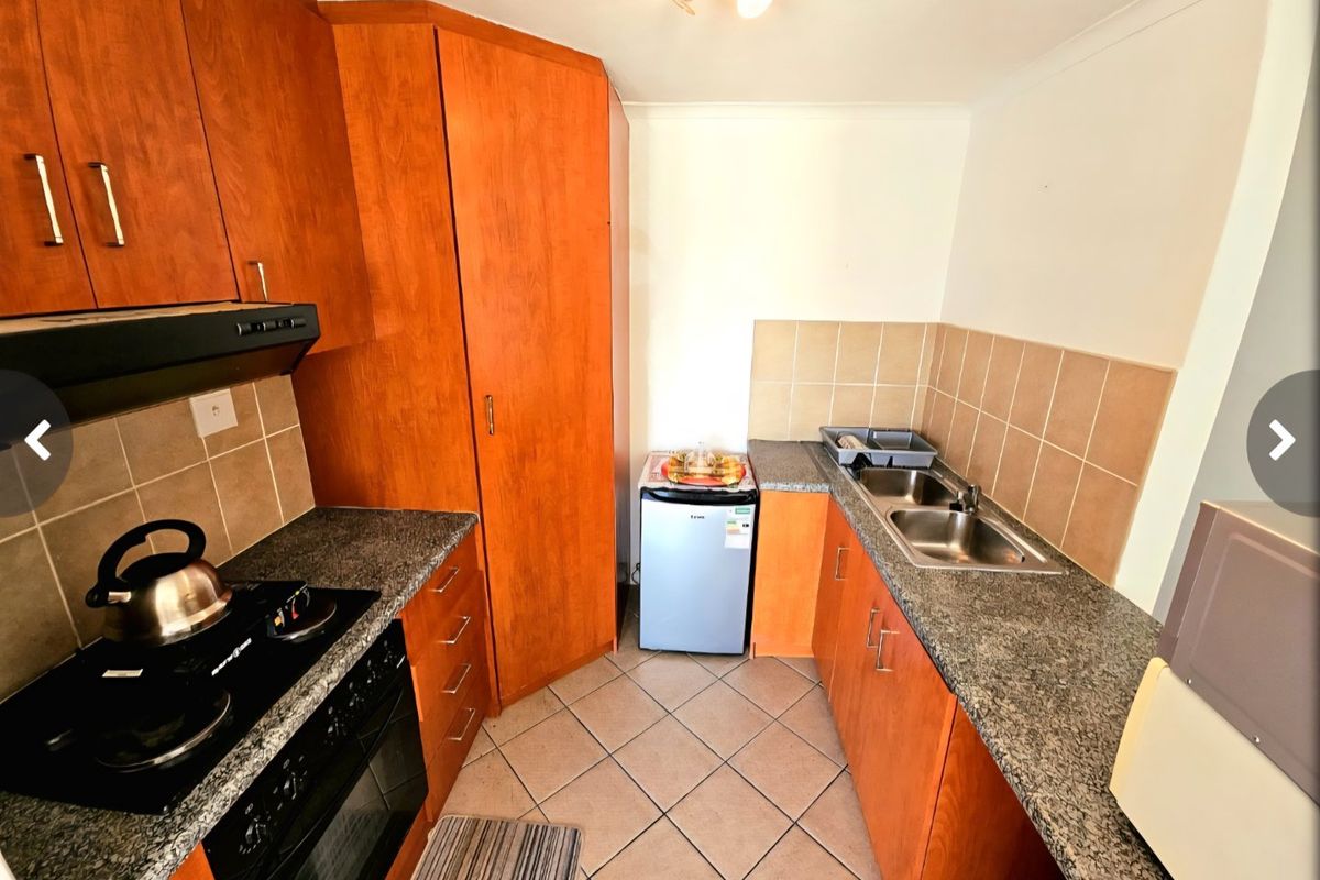A functional kitchen featuring wood-finish cabinetry, granite countertops, a stainless steel double sink, and built-in cooking appliances with a tiled backsplash.