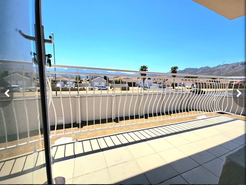 A spacious balcony featuring tiled flooring and a decorative metal balustrade, offering clear views of the surrounding neighborhood and mountain landscape.