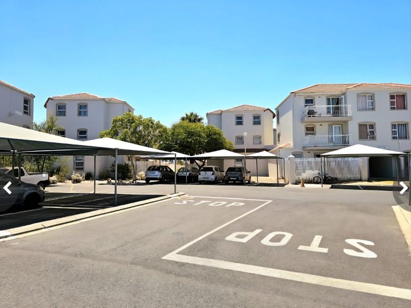 Exterior view of an apartment complex featuring paved parking areas with shade-cloth carports and multi-story residential buildings with balconies.