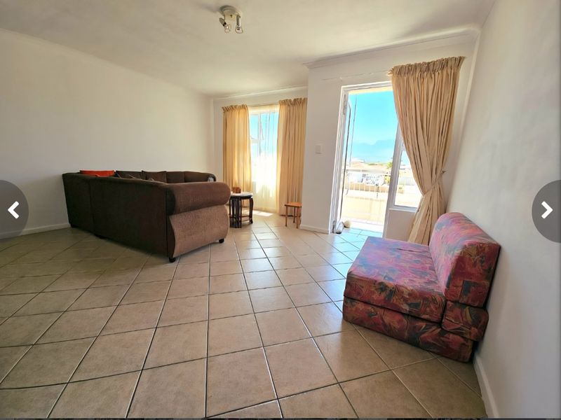 A spacious living room featuring ceramic tile flooring and direct access to a balcony through a sliding glass door.